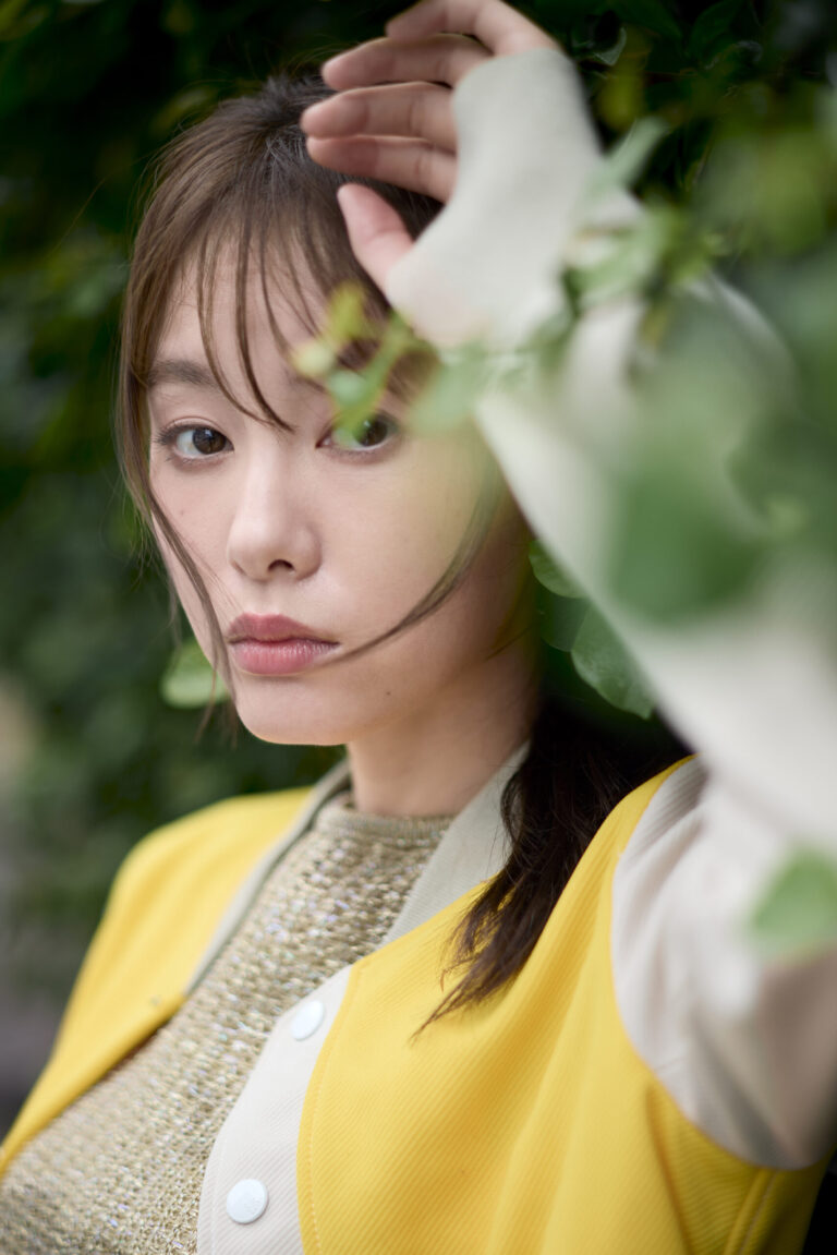 葉と腕の間からまっすぐこちらを見つめる渡部りおのポートレート